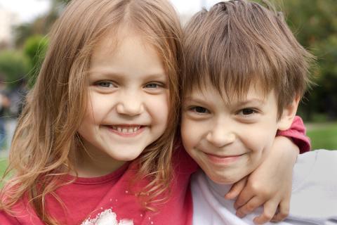 A young girl wraps her arm lovingly around her brother as they play together outside.