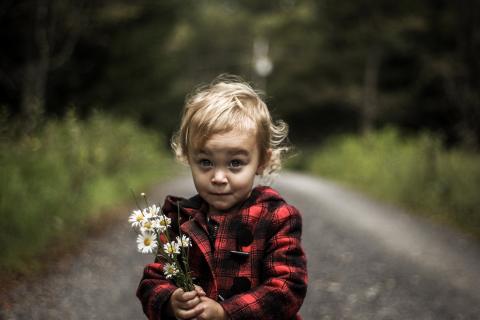 Little girl holding flowers looks playfully at the camera