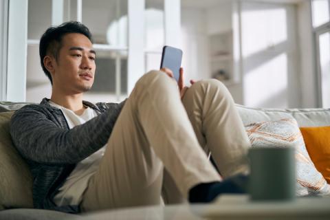 Man sits on the couch with a concerned look on his face while looking at a smartphone