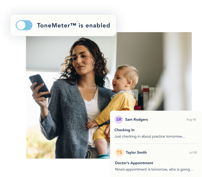 A mother holds her infant child with one arm while she looks at her cell phone in her other hand.