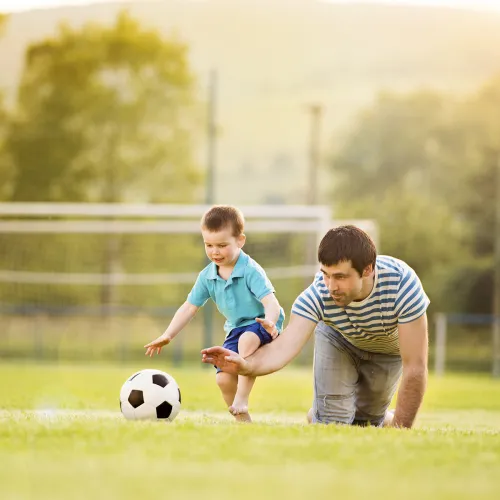Man and young boy play with a soccer ball on a field.