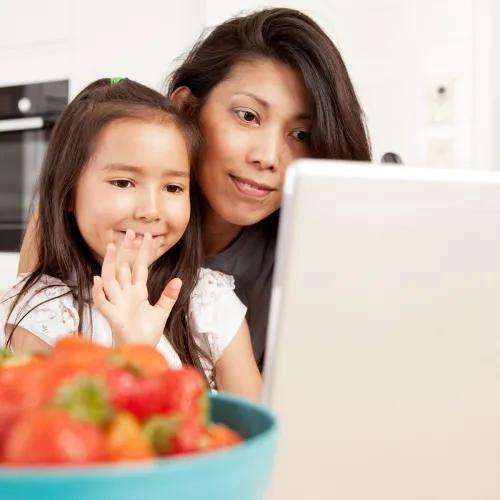 Child waving at parent on video chat while being held by mother
