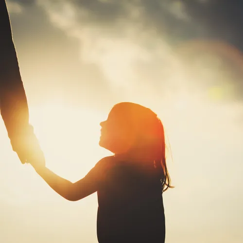 Silhouette of young girl looking up lovingly at parent while holding their hand.