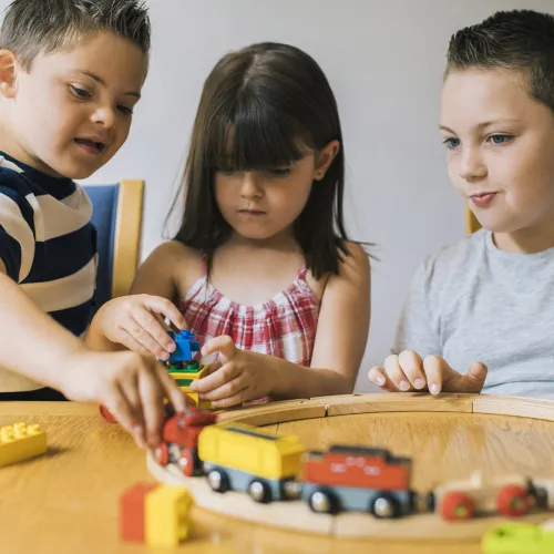 Three siblings sit at an activity table and play with a heap of educational toys.