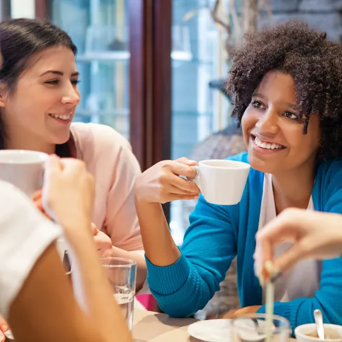 Four friends sit chatting at a table in a coffee shop.