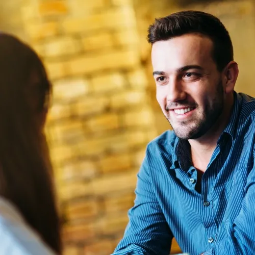 A man in a blue shirt smiling at a woman who is facing him.
