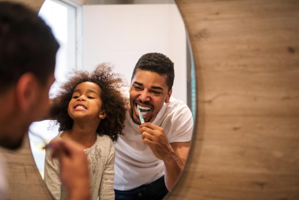 Father teaching daughter how to brush teeth