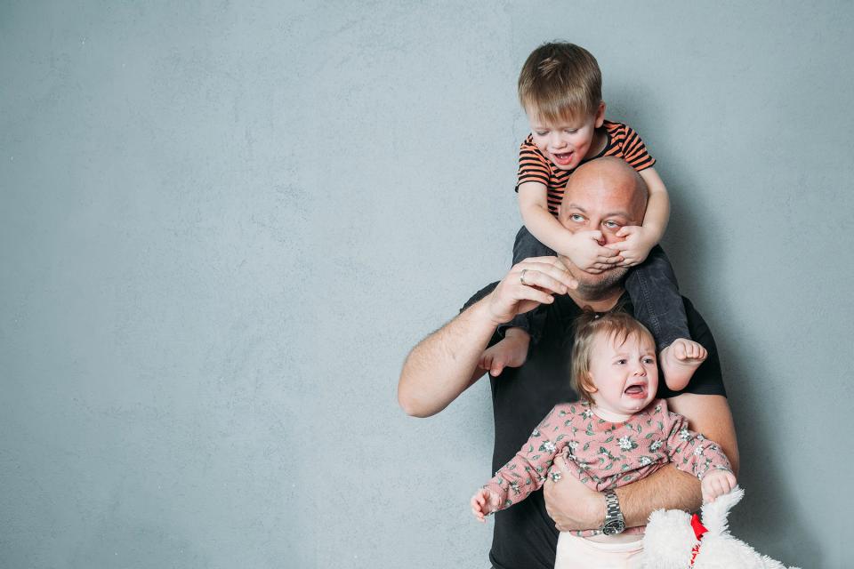 Father holds crying toddler as son crawls on his back