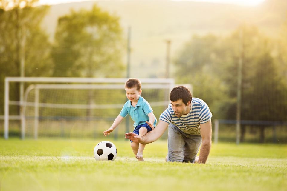 Man and young boy play with a soccer ball on a field.