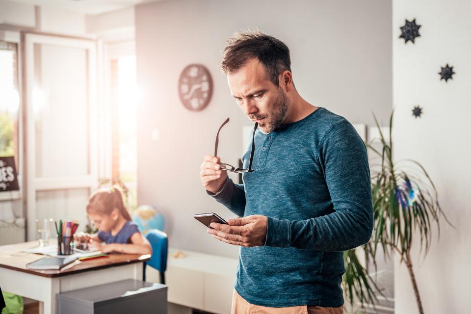 Father considers how to respond to a message on his phone while his daughter works on her homework.