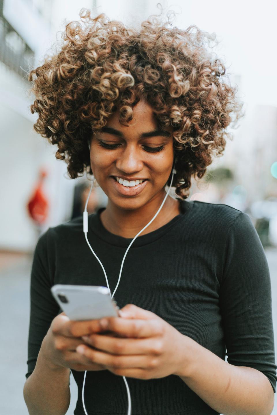 Teenaged girl wearing headphones smiles at phone while texting.