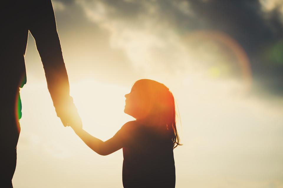 Silhouette of young girl looking up lovingly at parent while holding their hand.