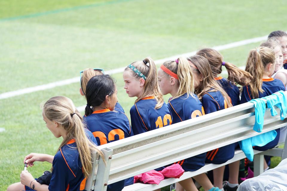 Girls sit on bench during soccer practice.