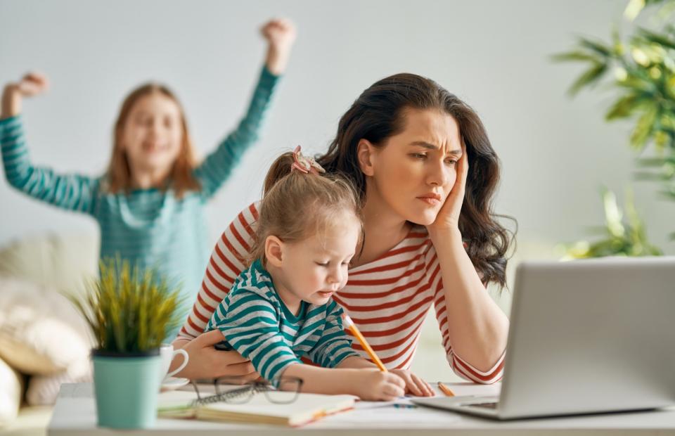 A busy mother looks worried at her computer as her children play around her.