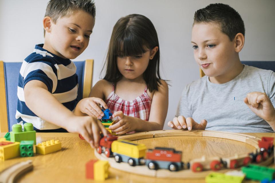 Three siblings sit at an activity table and play with a heap of educational toys.