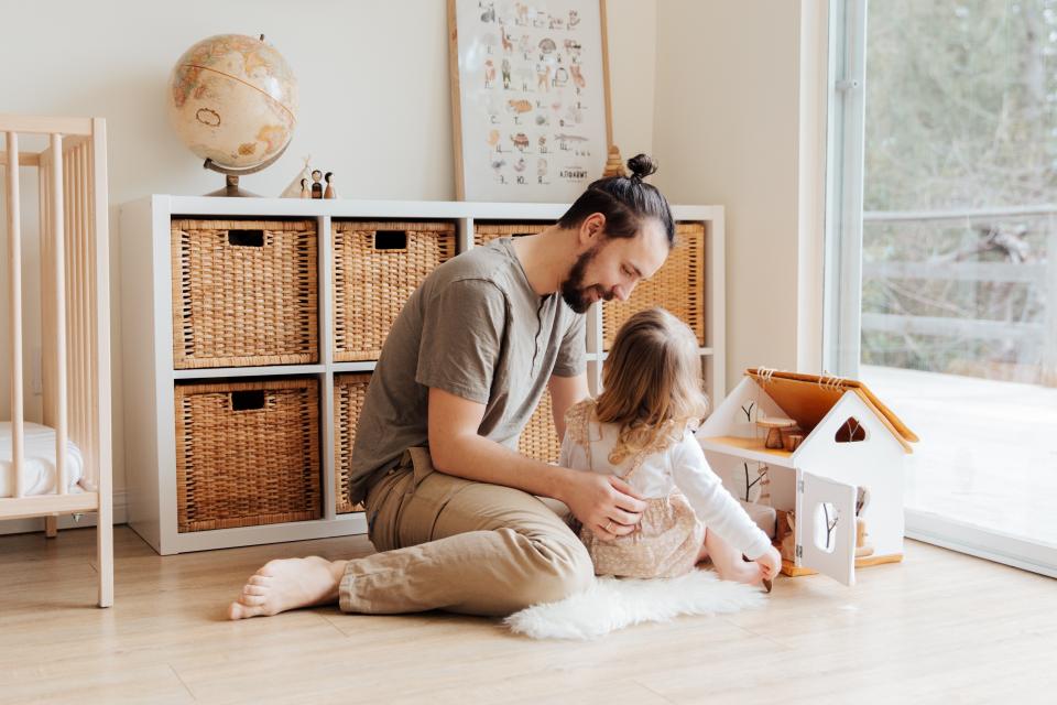 A father and his daughter play together with a doll house.