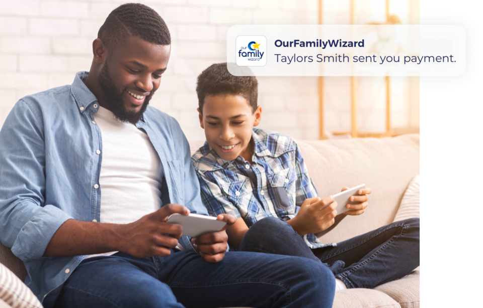 Father and son sit on a couch, each holding a smartphone. The son looks at his Dad's phone to see a push alert about a payment.